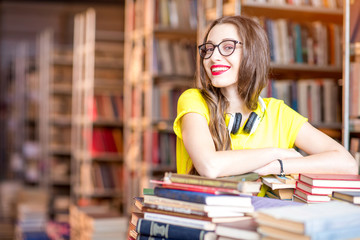 Portrait of young enthusiastic female student studying with a lot of books at the library