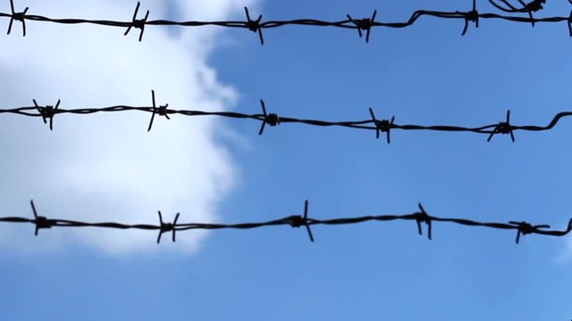 Blue sky and clouds behind the barbed wire. Close up