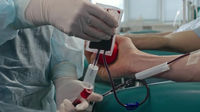 Closeup of man squeezing stress ball while nurse placing bag attached to evacuated collection tube system during process of donating blood