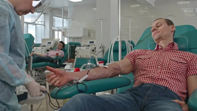 Nurse taking off needle with evacuated collection tube system from arm of patient after blood drawing in donation center
