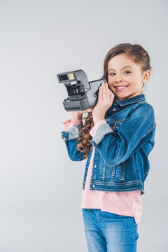 Adorable girl taking pictures on retro camera on gray