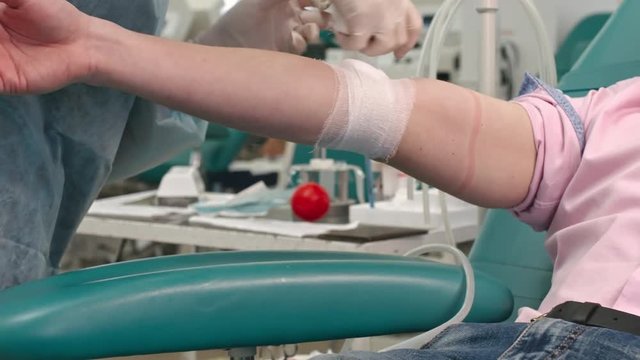 Closeup of nurse wrapping sterile gauze around arm of patient after blood transfusion procedure in donation center