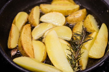 Potato slices fried in oil in a frying pan with rosemary