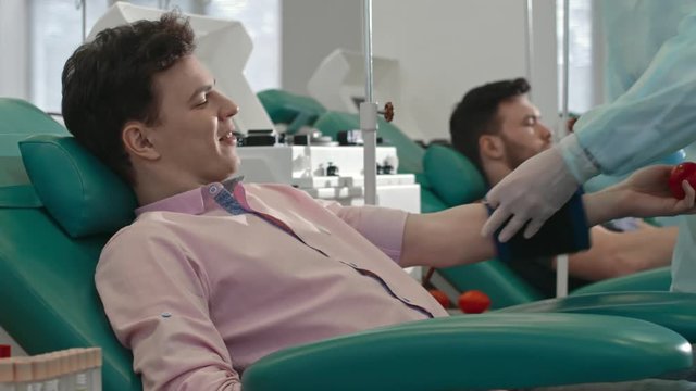 Young man smiling and talking to doctor while he putting tourniquet on arm before obtaining blood