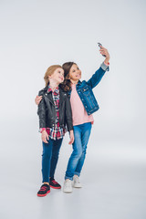 Fototapeta premium Adorable smiling little girls taking selfie with smartphone on grey