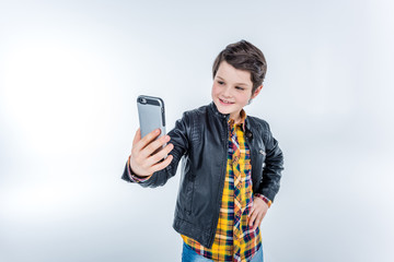 portrait of stylish smiling boy making selfie on grey