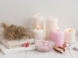 Spa composition with candles, sea salt and flowers on white wooden background.