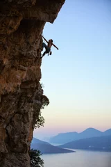 Fototapeten Young man climbing vertical cliff at sunset © Andrey Bandurenko