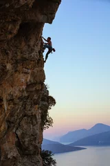 Foto op Aluminium Young man climbing vertical cliff at sunset © Andrey Bandurenko