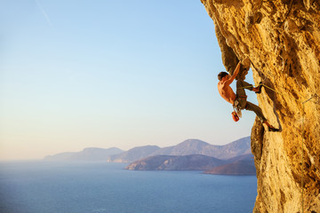 Young man struggling to climb challenging route on cliff