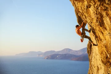 Schilderijen op glas Young man struggling to climb challenging route on cliff © Andrey Bandurenko