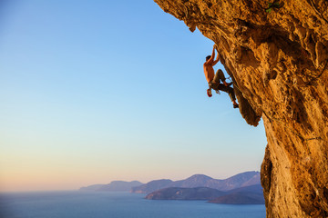 Young man struggling to climb challenging route on cliff at sunset