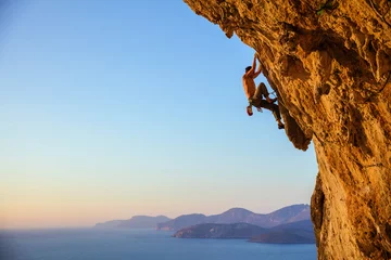 Gordijnen Young man struggling to climb challenging route on cliff at sunset © Andrey Bandurenko