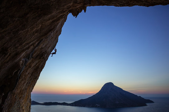 Rock climber on overhanging cliff at sunset