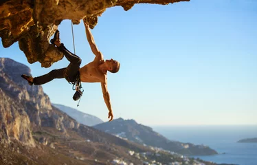 Fotobehang Young man struggling to climb ledge on cliff © Andrey Bandurenko