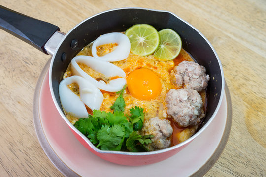 Spicy soup with soft boiled egg, meat ball and squid. It is topped with parsley and sliced lemons.