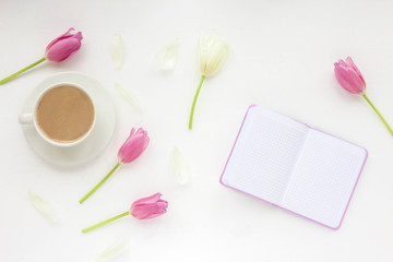 Flowers composition. Woman's workspace wiht notebook, cup of coffee white and lilac tulip, pen on white background. Flat lay, top view