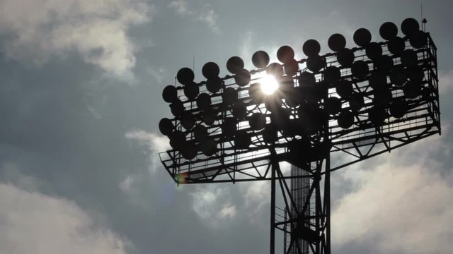 Sun shines through the stadium lights against the background of moving clouds. Time-laps