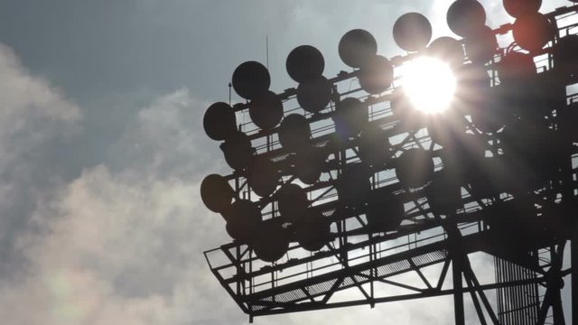 Sun shines through the stadium lights against the background of moving clouds. Time-laps