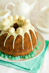 Glazed Easter cake decorated candy eggs on white wooden table. Selective focus
