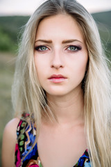 beautiful dreamy blonde girl with blue eyes in a light turquoise dress lying on the stones