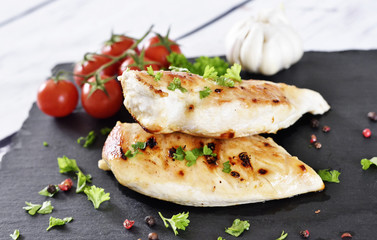 Grilled chicken breast on a slate plate with herbs and cherry tomatoes, garlic and peppercorns. Healthy eating scene, barbecue chicken.