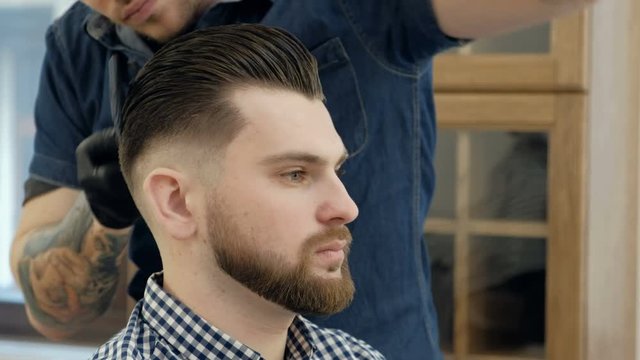 Male barber in plaid shirt combing hair of a male client at barbershop