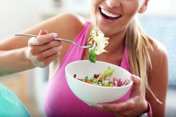 Young woman eating healthy salad after workout - obrazy, fototapety, plakaty