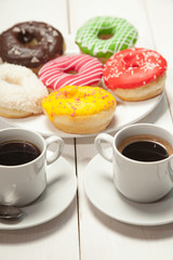 Two cups with coffee and donuts on a white wooden table