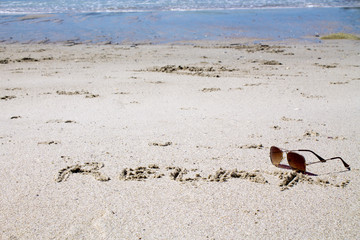Sunglasses and words on the sand of the beach