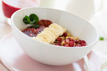 Healthy breakfast: muesli with walnuts, milk, honey, banana, orange and garnet seeds on white wooden background. Selective focus
