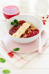 Healthy breakfast: muesli with walnuts, milk, honey, banana, orange and garnet seeds on white wooden background. Selective focus

