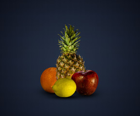 Pineapple, lemon, orange and apple isolated on dark blue background
