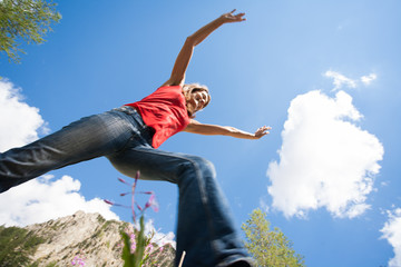 femme souriant en contre plongée qui saute dans les montagne en été