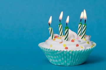 Cupcake mit weißer Creme und grünen Kerzen auf blauem hintergrund