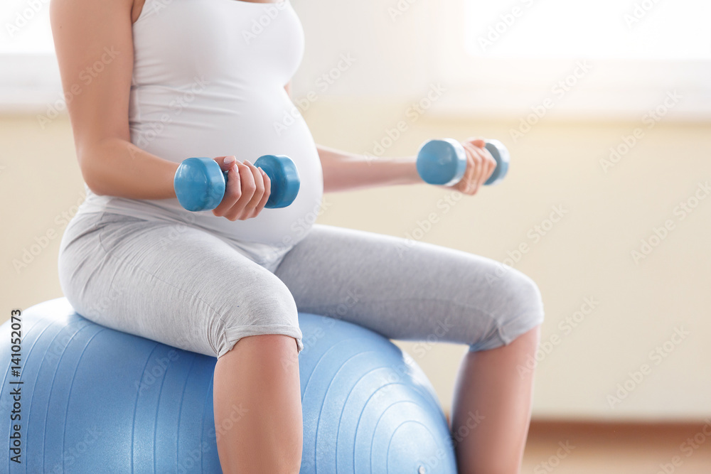 Wall mural portrait of a beautiful young pregnant woman executing exercises with fitball