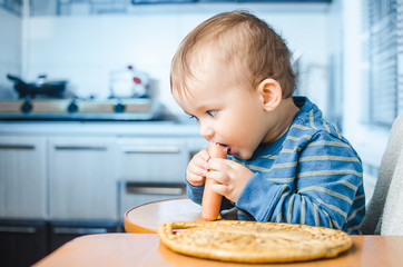 The child in the kitchen eating sausage