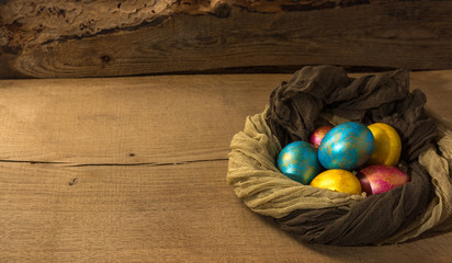 Multi-colored Easter eggs in a nest of soft scarf on a natural wooden background. Copy space.