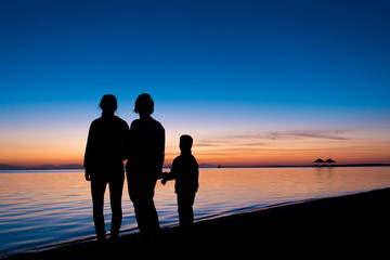 silhouette of three people standing on the beach in sunrise