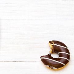 Tasty bitten donuts with icing and chocolate on white wooden background, copy space