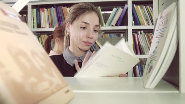 Female student among bookcases in library looking for books