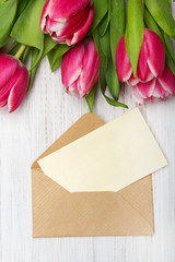 Tulip bouquet and envelope on white wooden background, copy space