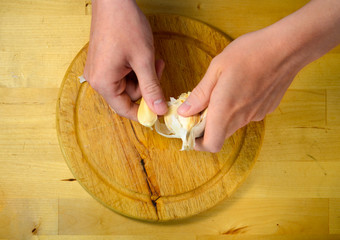 cooking and home concept - close up of male hands taking off peel of garlic on cutting board - 141056257