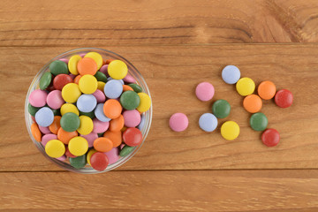 Caramelos de chocolate y colores diversos en un bol de cristal sobre fondo de madera marrón