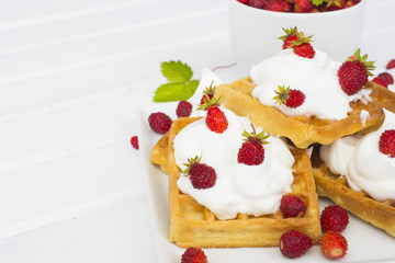 waffles with wild strawberries and whipped cream on white table