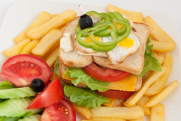 club sandwich on a white plate with french fries and vegetables