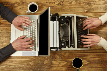 Woman writing on a typewriter and a man working on a laptop.