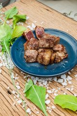 Medium Rare Fried Diced Marinated Beef on Blue Ceramic Plate on Wood Panel with Sea Salt and Vegetable Decorated.