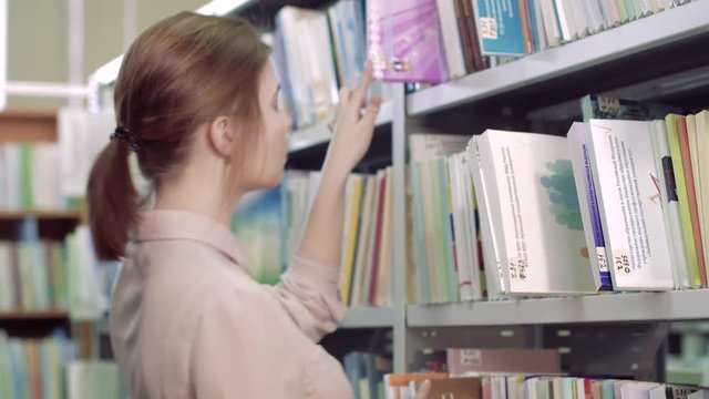 Close-up of focused female student in library trying to find a necessary book on bookcases