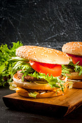 Freshly homemade burgers with cheese, beef minced steak, tomato and lettuce. On the black concrete background, with vegetables, copy space